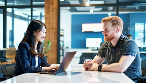 In a modern tech office characterized by sleek furniture and vibrant decor an Asian woman and a white male sit across from each other at a large polished conference table The woman dressed in a smart blazer is animatedly presenting her ideas on the n-3